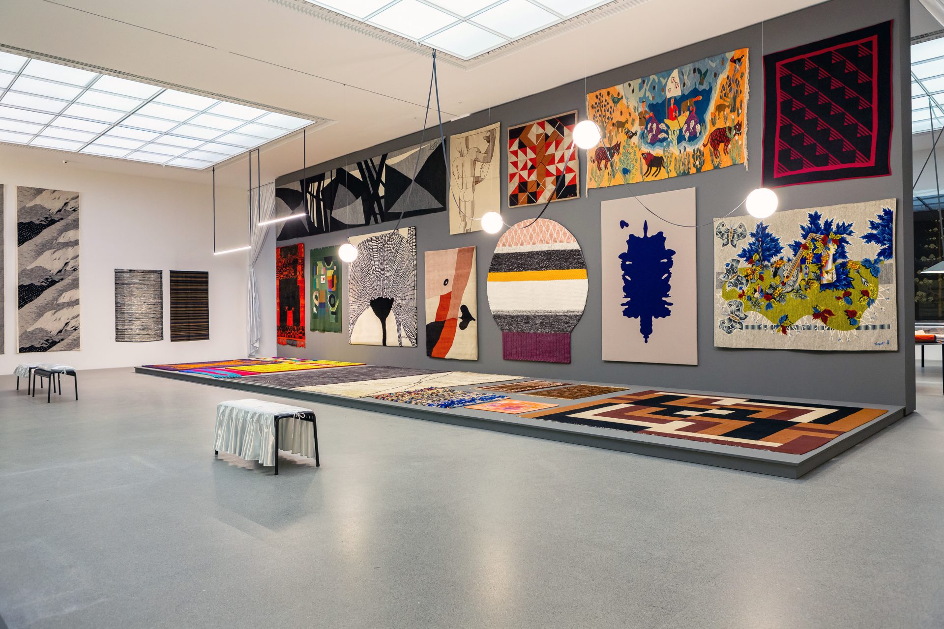 Wall with textiles of different size, laying textiles. Benches for visitors