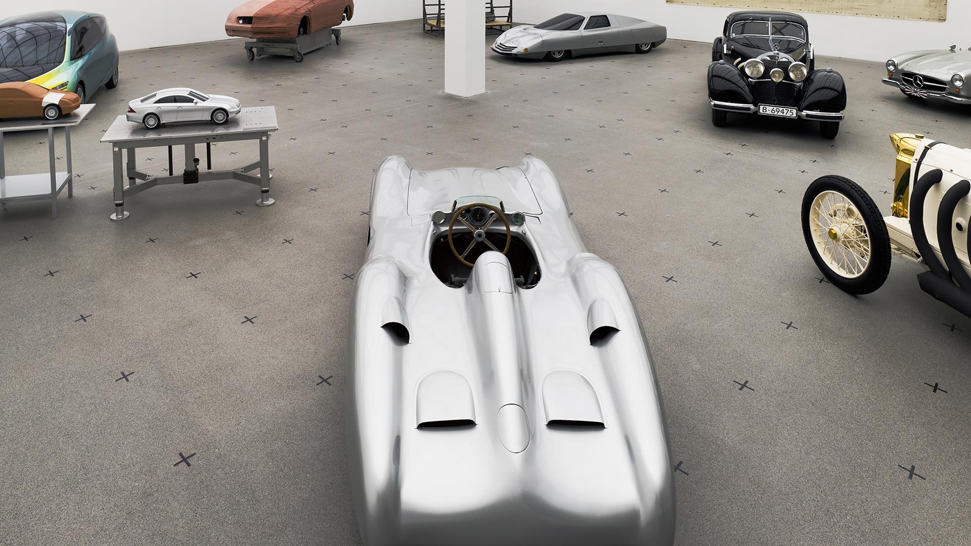 Blick in die Ausstellung "Meilensteine. Automobil-Design. Mercedes-Benz" aus der Vogelperspektive. Zu sehen sind 7 verschiedene Automobile sowie 2 Miniaturen auf Podesten.