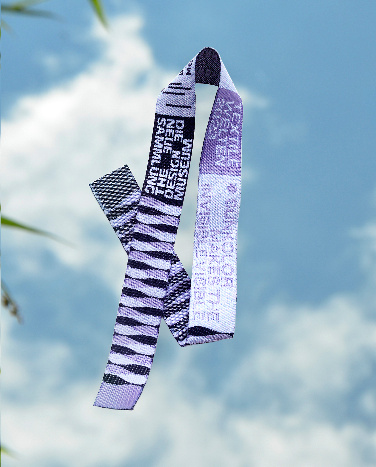 Edited photo. A black, purple and white ribbon of plastic fibre floats above a sunny cloudy sky.
