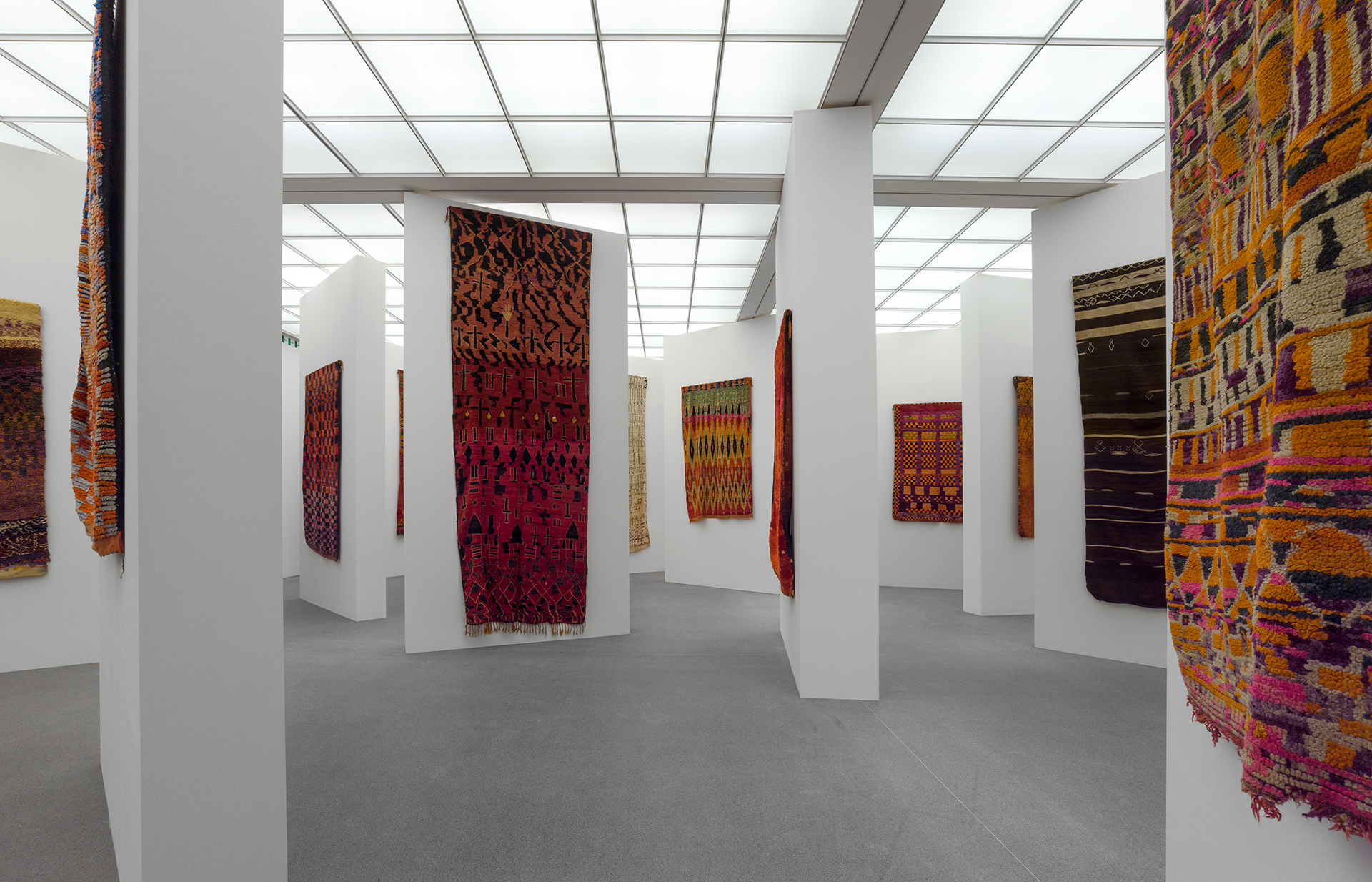 Exhibition room with walls spread out and artfully woven carpets hanging from them.