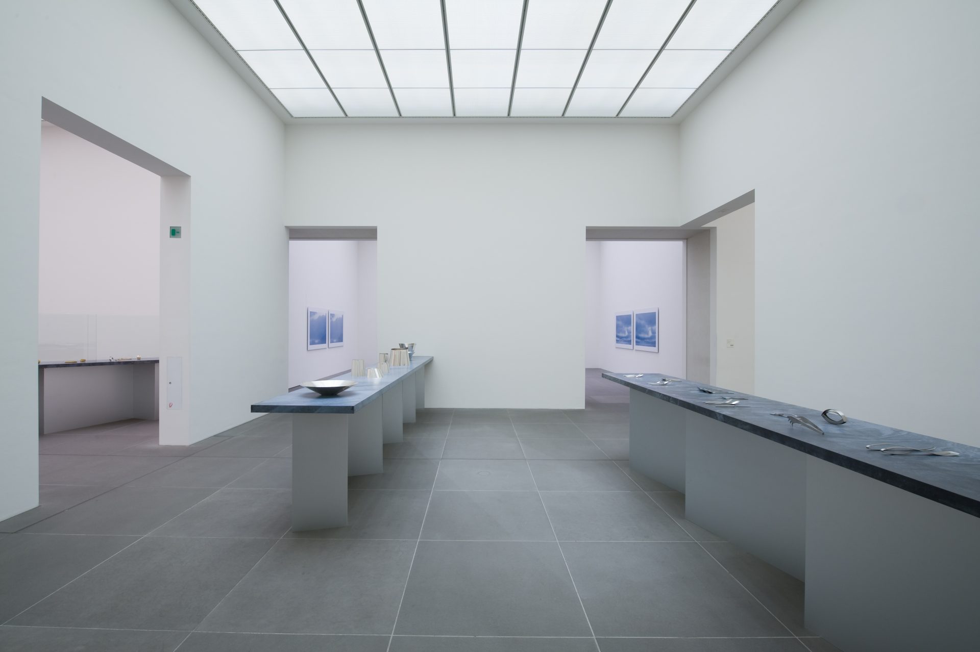 Frontal view of exhibition room, left with silver vessels, right silver cutlery on blue pedestal.