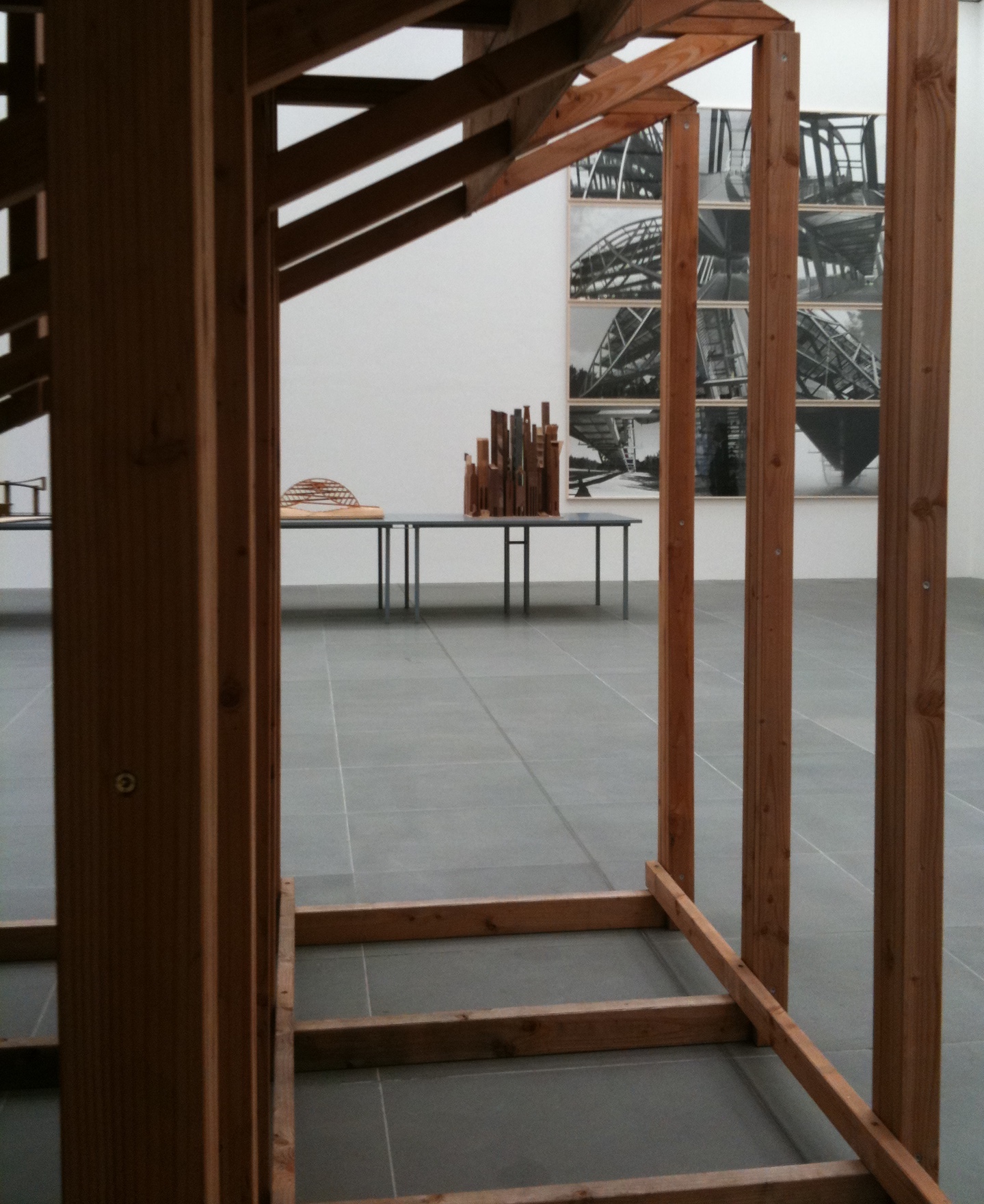 Close-up of a wooden construction. Photographs of scaffolding and wooden models in the background.