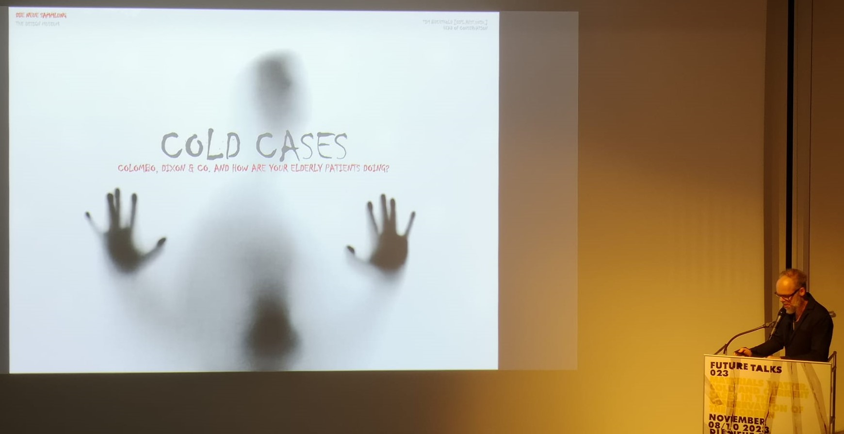 Der Leiter der Restaurierung, Tim Bechtold, steht auf einer Bühne hinter einem Podest. Im Hintergrund sieht man eine helle Projektion mit der Aufschrift "Cold Cases". Das war das Thema der Future Talks 2023.