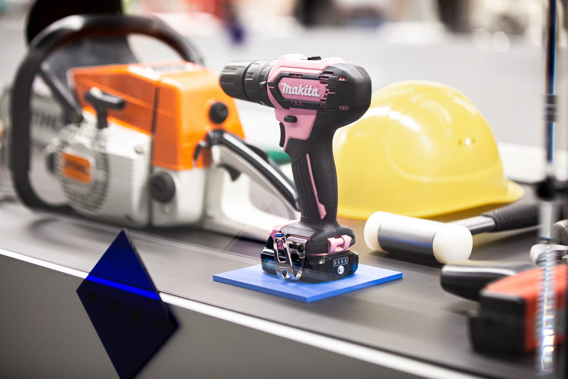 Pink cordless drill in a display case is highlighted by a blue base and blue diamond on the display case.