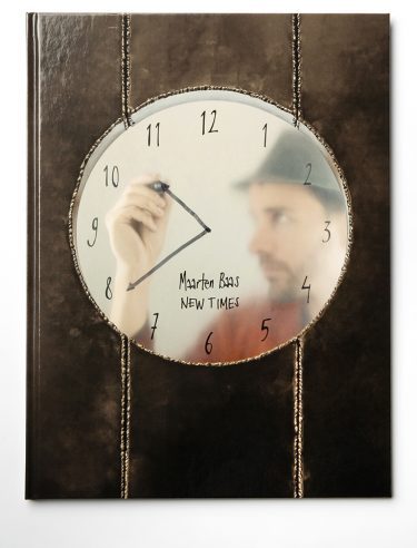 Cover Ausstellungskatalog. Zu sehen ist ein rundes Zifferblatt einer Uhr. Darin befindet sich ein Mann mit Hut, der die Zeiger von Innen an die Glasscheibe schreibt.