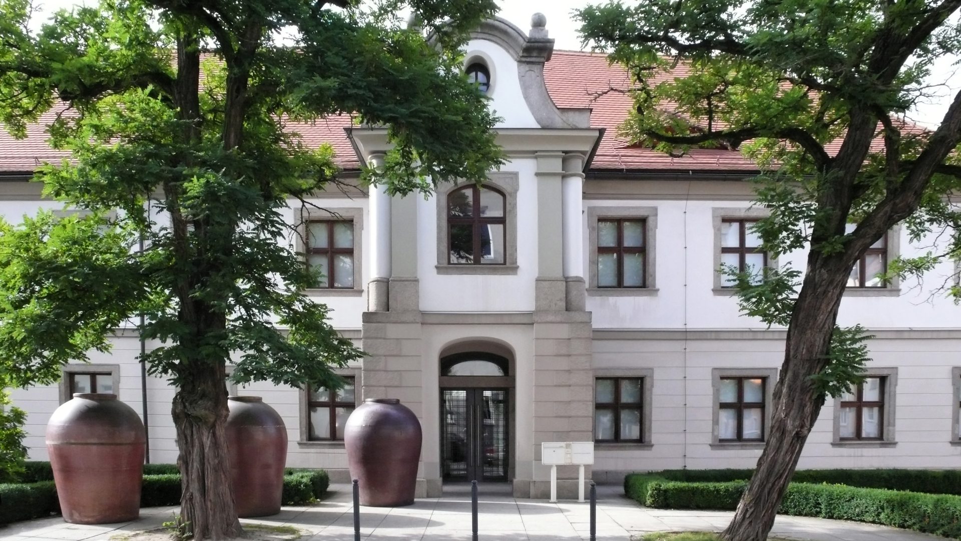 Außenansicht Museum Weiden, Eingang: grau-weißes Gebäude aus dem Neo-Barock mit Bäumen davor