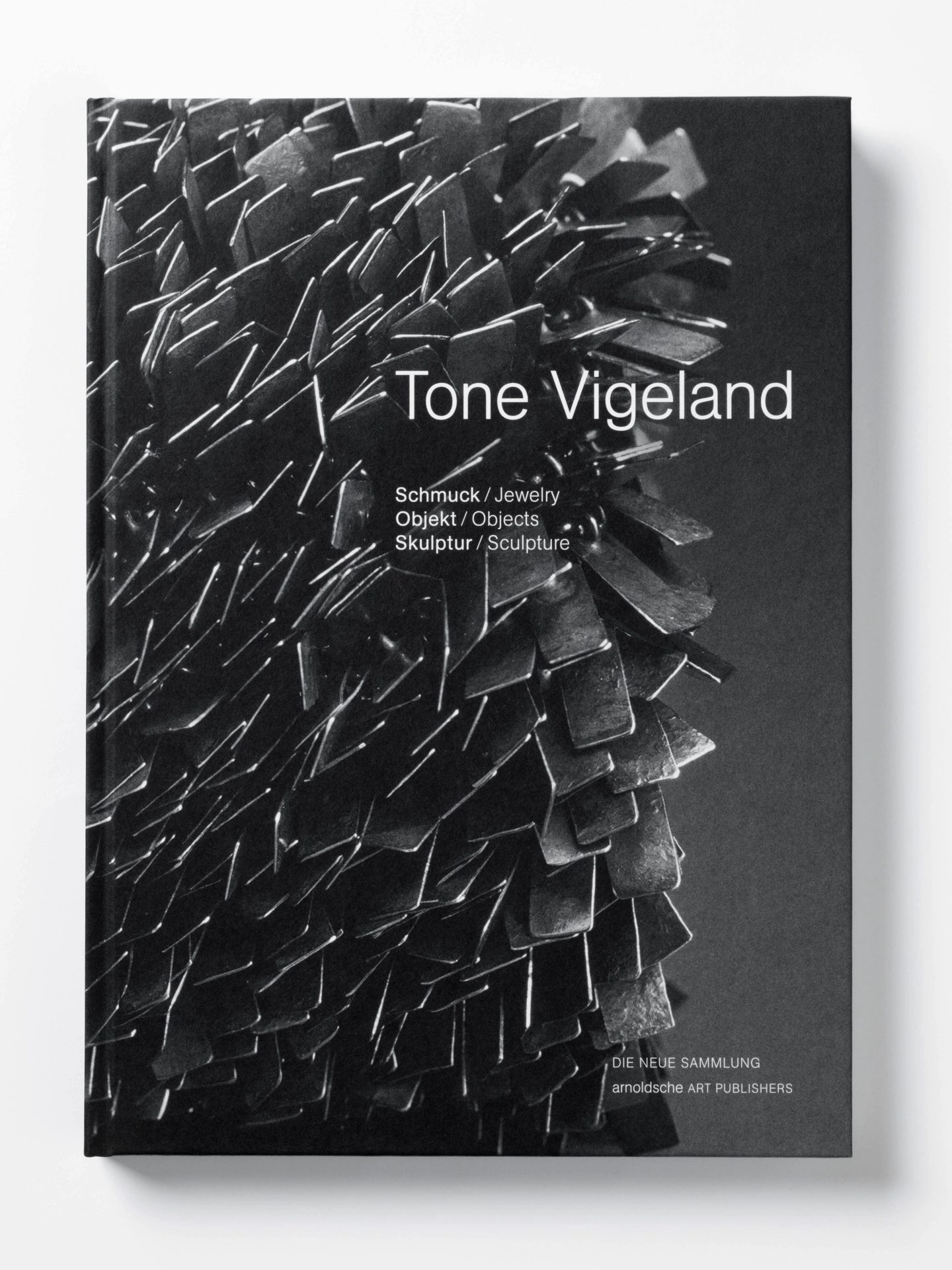 Cover of the exhibition catalogue. Black and white photograph of metal sheets on the left edge of the book. Above it is written in white, thin lettering Tone Vigeland.