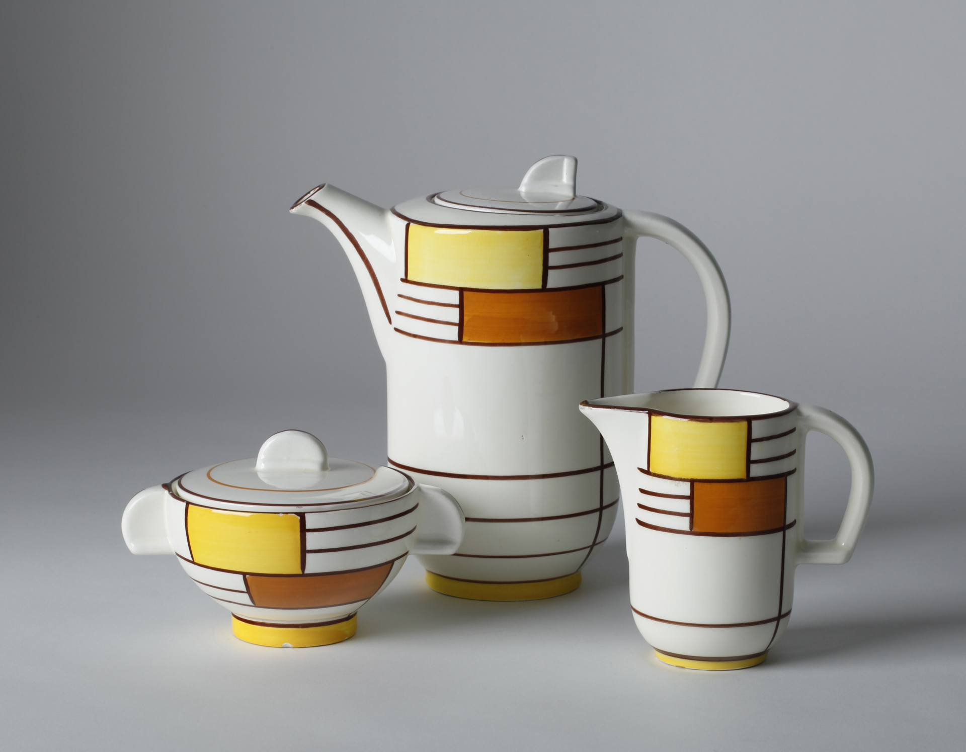A three-piece white tea service with orange and yellow painting.