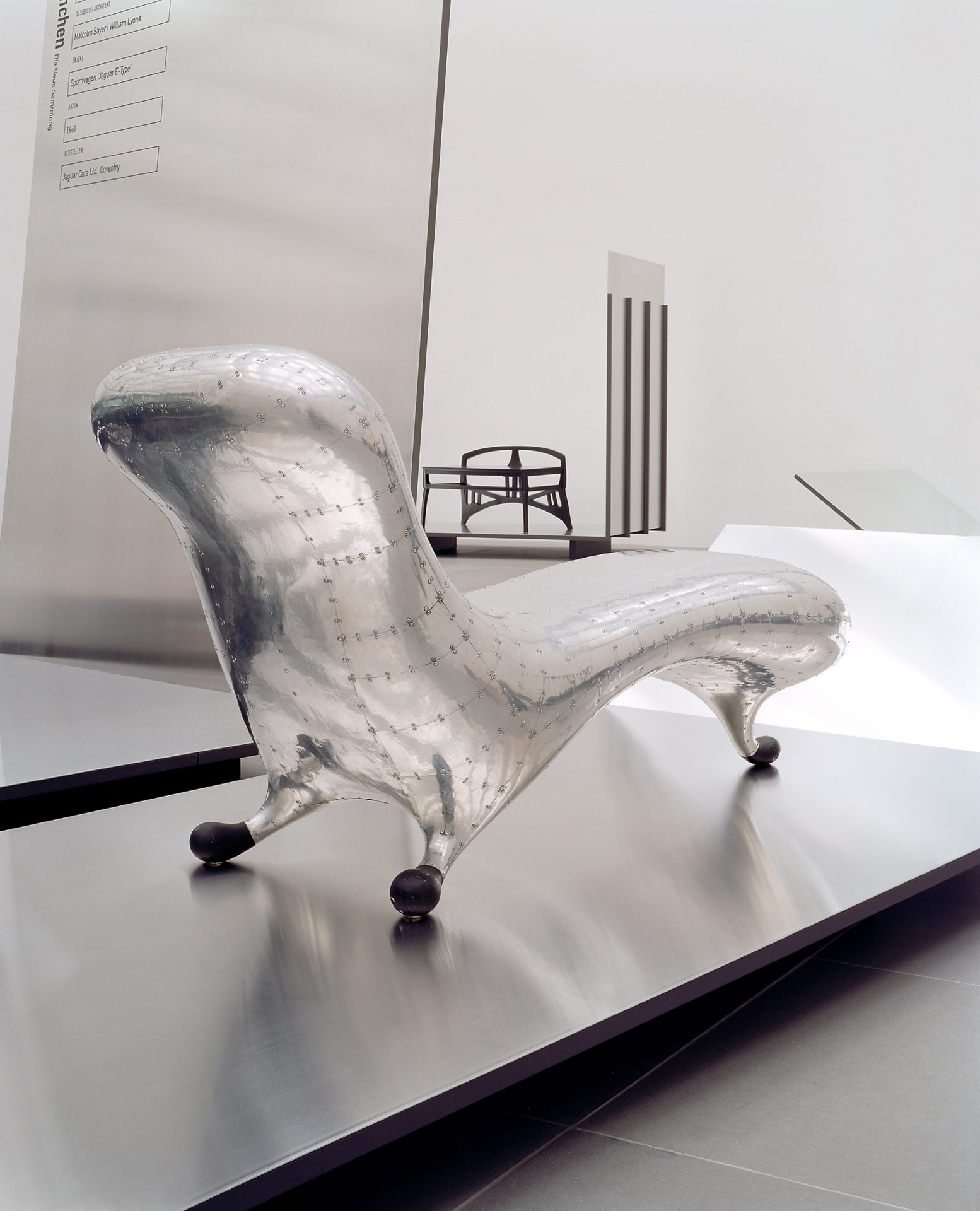 Ein silberfarbenes Sitzmöbel aus Metall mit schwarzen Füßen.