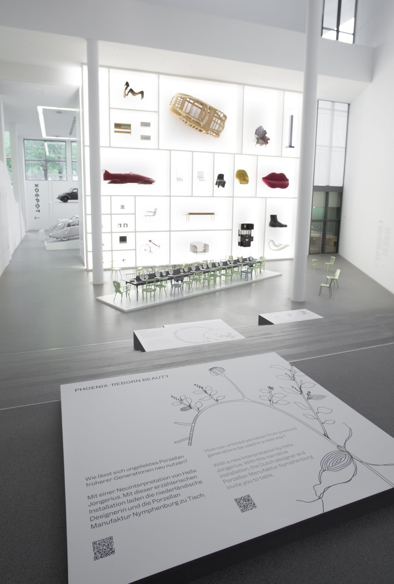 View of the Hella Jongerius installation, text plinth on the stairs and table with chairs in front of a shelf with design objects