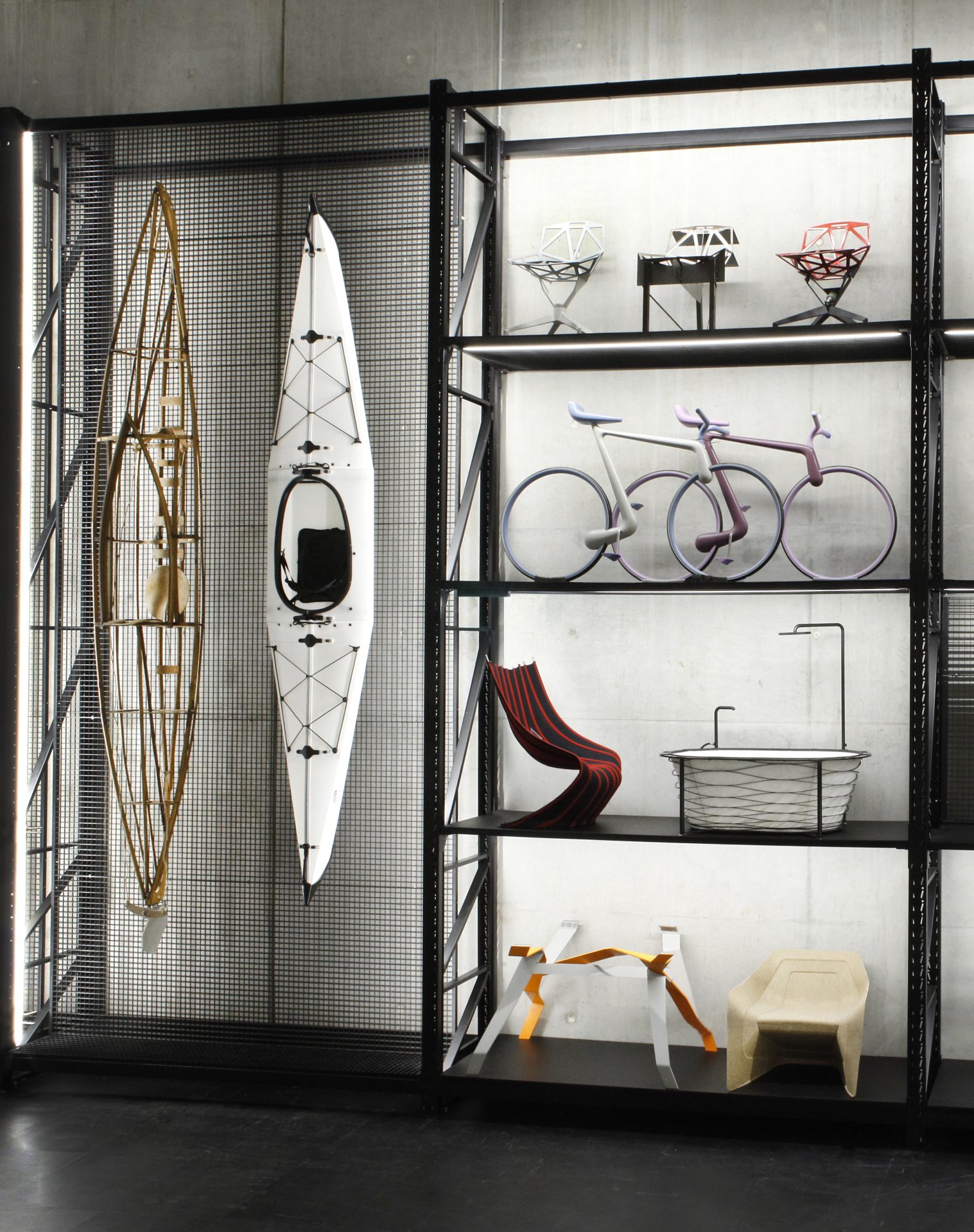Zu sehen ist ein Schwerlastregal mit auf der linken Seite zwei Kanus und auf der rechten Seite Stühlen in verschiedenen Formen sowie an Fahrräder erinnernde Objekte.