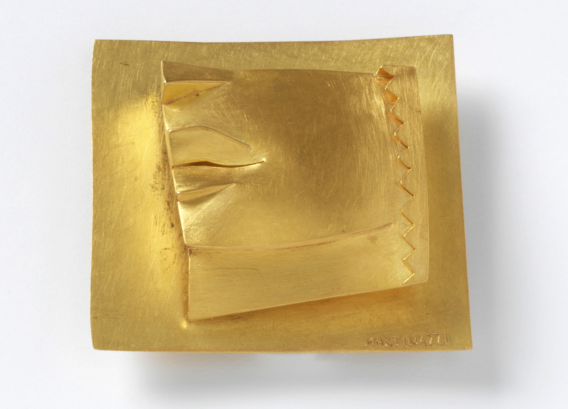 Photo of gold jewellery. Two square sheets are placed on top of each other. The upper, smaller rectangle has a jagged edge on the right which is turned into the centre of the surface.
