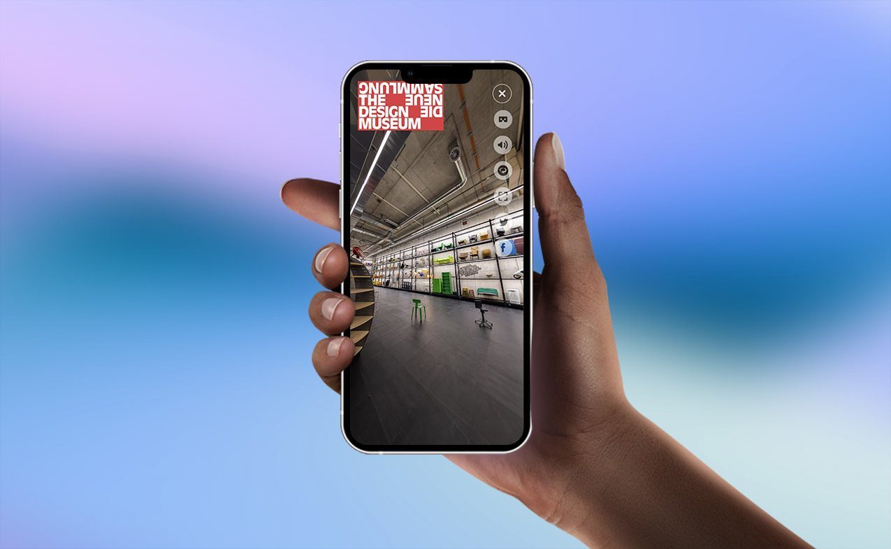 Werbefoto. Eine Hand hält ein Handy. Auf dem Bildschirm ist das digitale Abbild des Raums. Oben rechts befindet sich das Logo von Die Neue Sammlung.