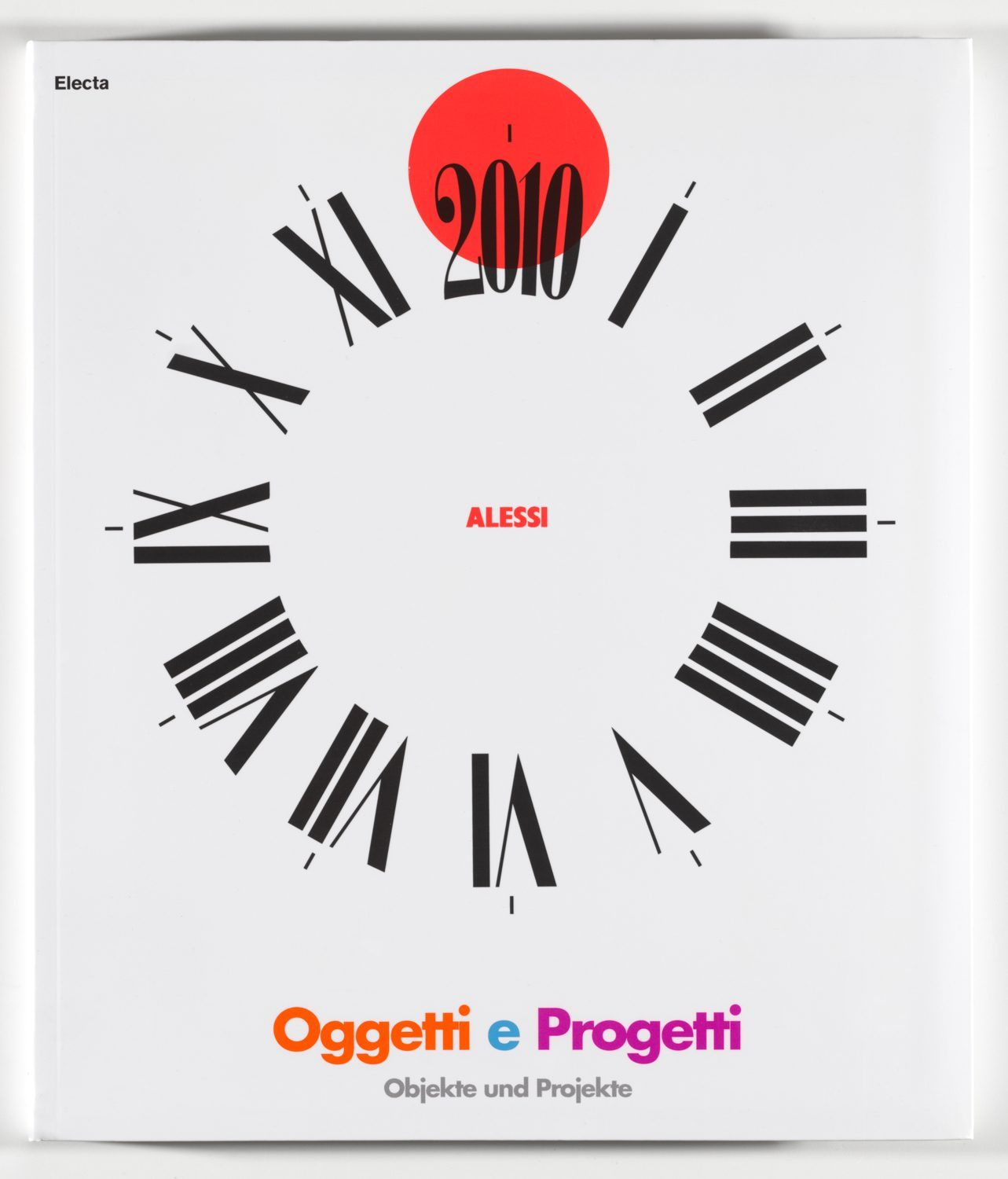 Black dial with Roman numerals on a white background. The 12 is replaced by 2010 on a red circle slightly shifted upwards. Inscription in red in the centre: Alessi. Inscription below, in orange, blue, pink and grey: Oggetti e Progetti. Objekte und Projekte.