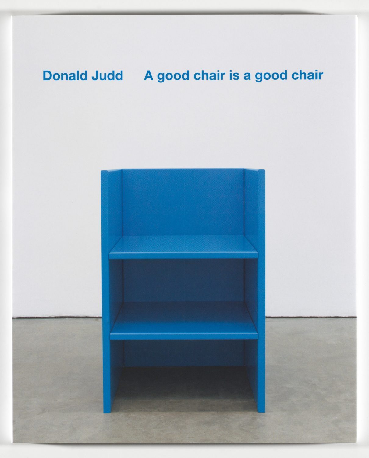 In einem Raum mit grauem Fußboden steht vor einer weißen Wand ein ultramarinblauer Stuhl, der aus drei vertikal ausgerichteten Brettern geformt ist, die durch zwei horizontale Bretter stabilisiert werden. Darüber Beschriftung in blau: Donald Judd A good chair is a good chair.