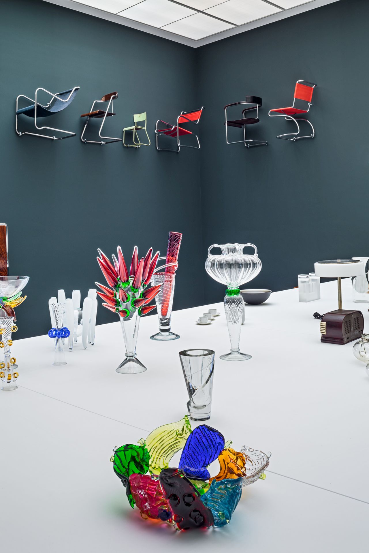 Chairs on the wall, glass objects on a white panel