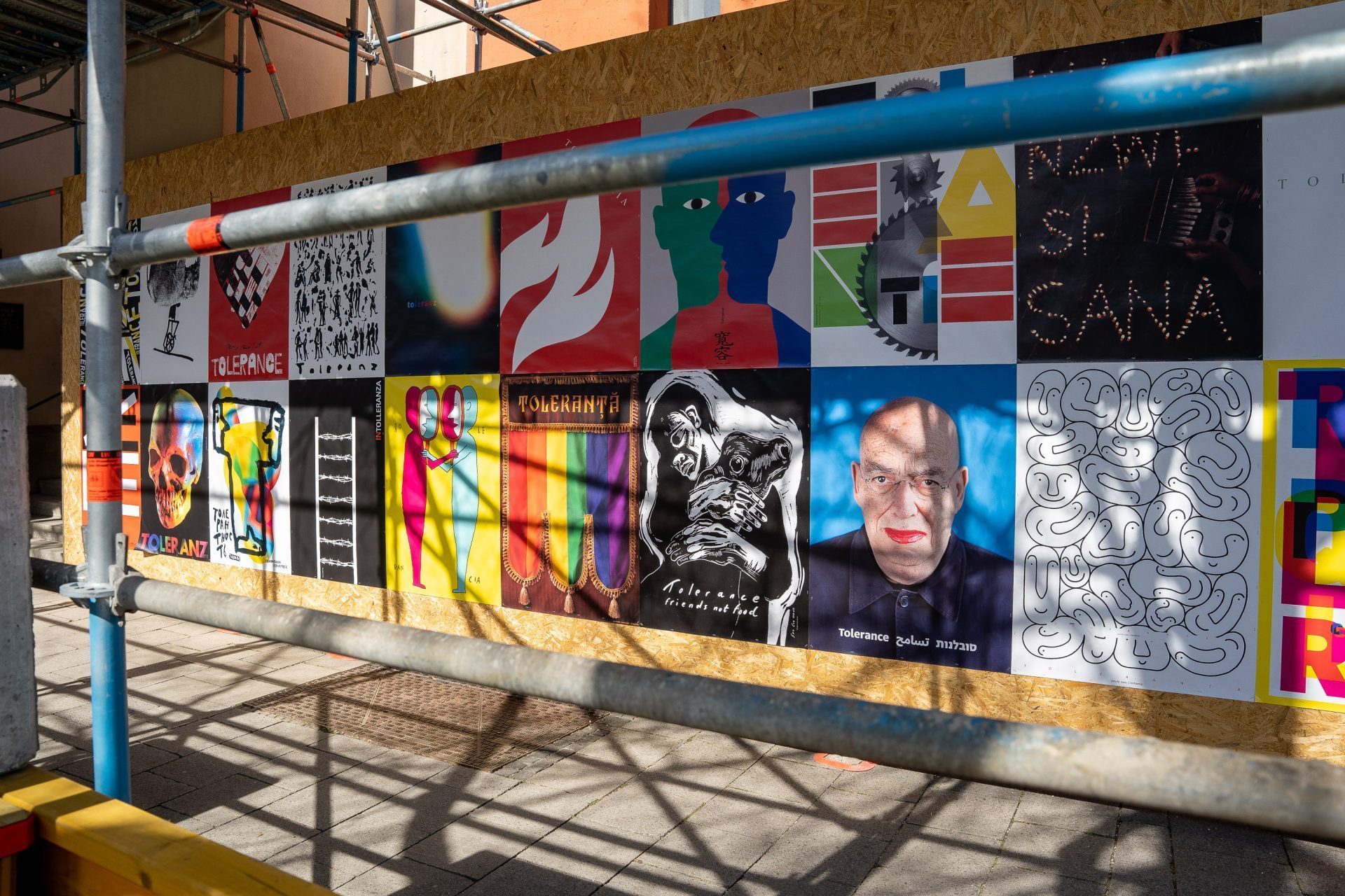 Poster wall on plywood panels, with scaffolding in front.