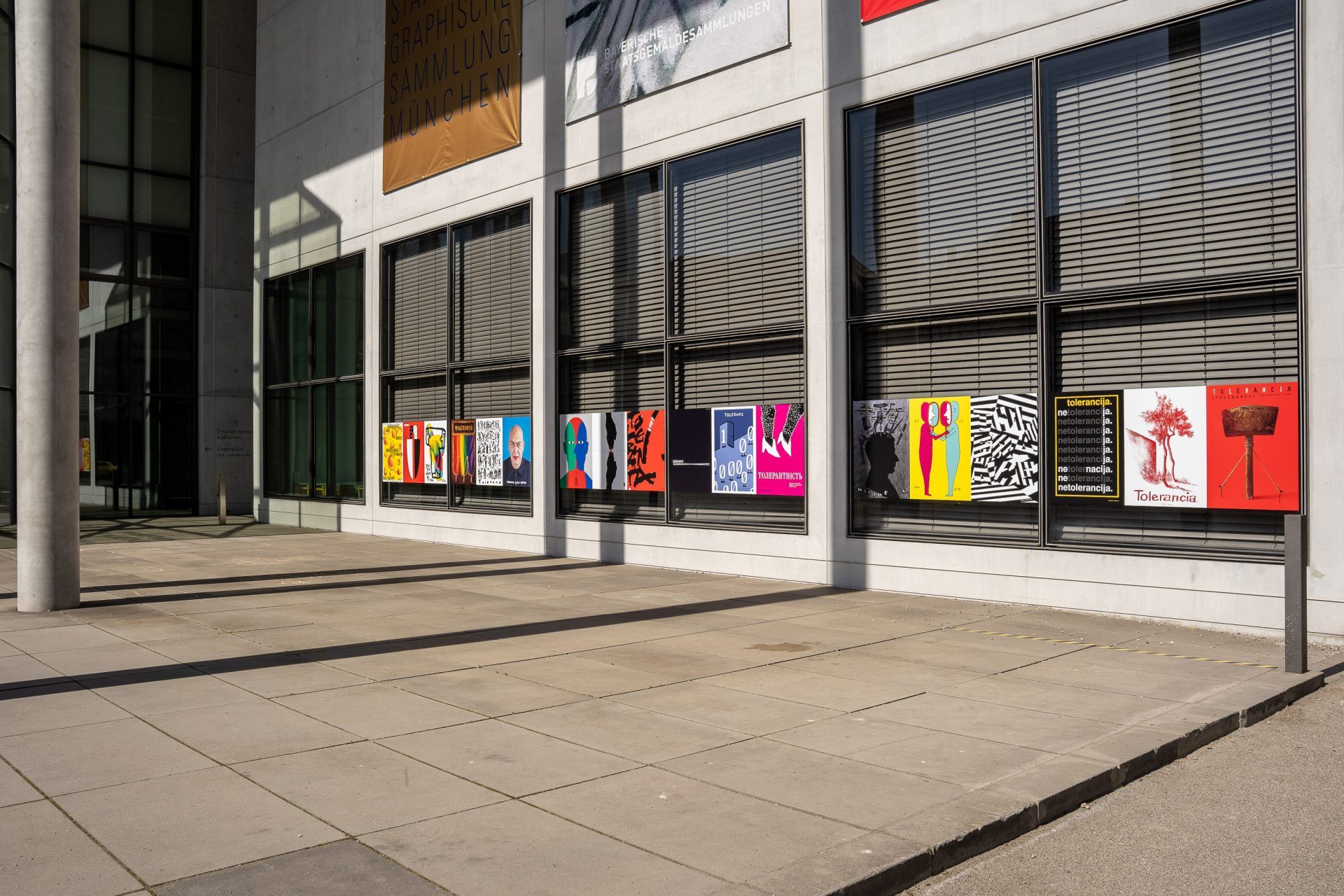 An der Fensterfront der Pinakothek der Moderne hängen Außen eine Reihe von bunten Plakaten.