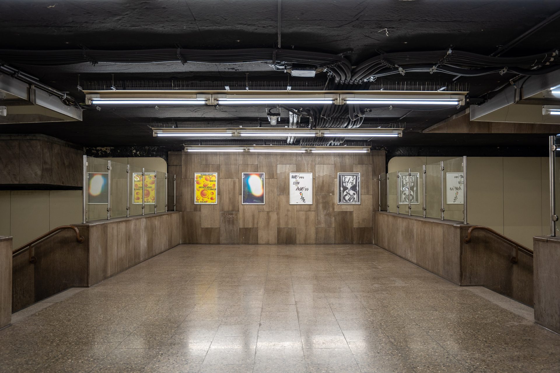 Four posters hang between two staircases. It is the interior of an underground station.