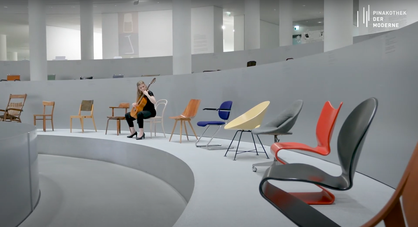 Laura Lootens with her guitar sitting on the chairs of the "Thonet & Design" exhibition in the Rotunda.