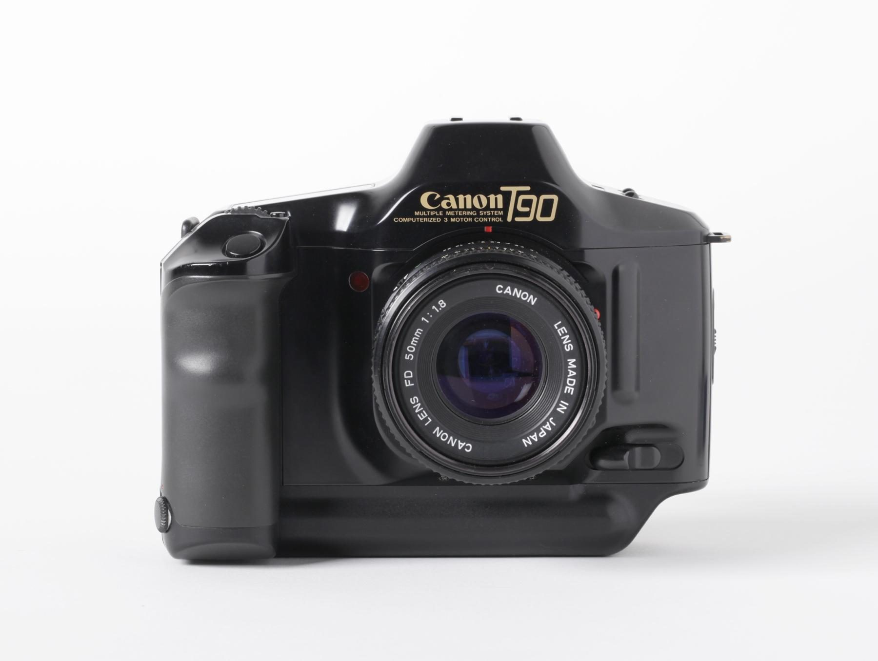 Frontansicht der Kamera mit schwarzem Gehäuse und Objektiv. Das Logo „Canon T90“ ist in goldener Schrift oben sichtbar, das Design wirkt robust und ergonomisch.