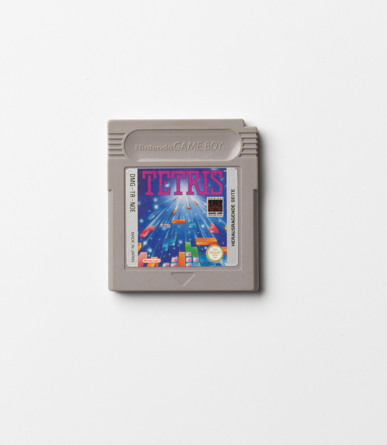 Grey Game Boy cartridge with the game ‘TETRIS’. The label shows the game title in pink lettering and an illustration of falling Tetris blocks in bright colours. 