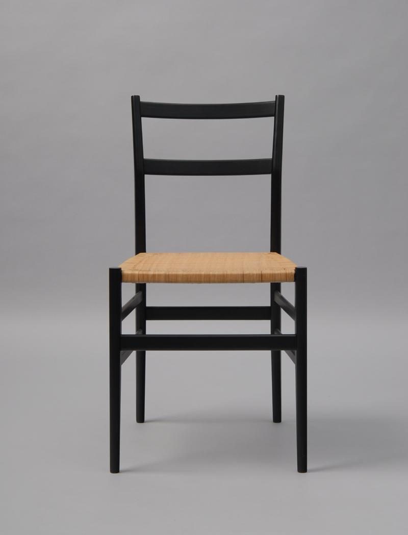 Frontal view of a black wooden chair with a woven seat, against a grey background.
