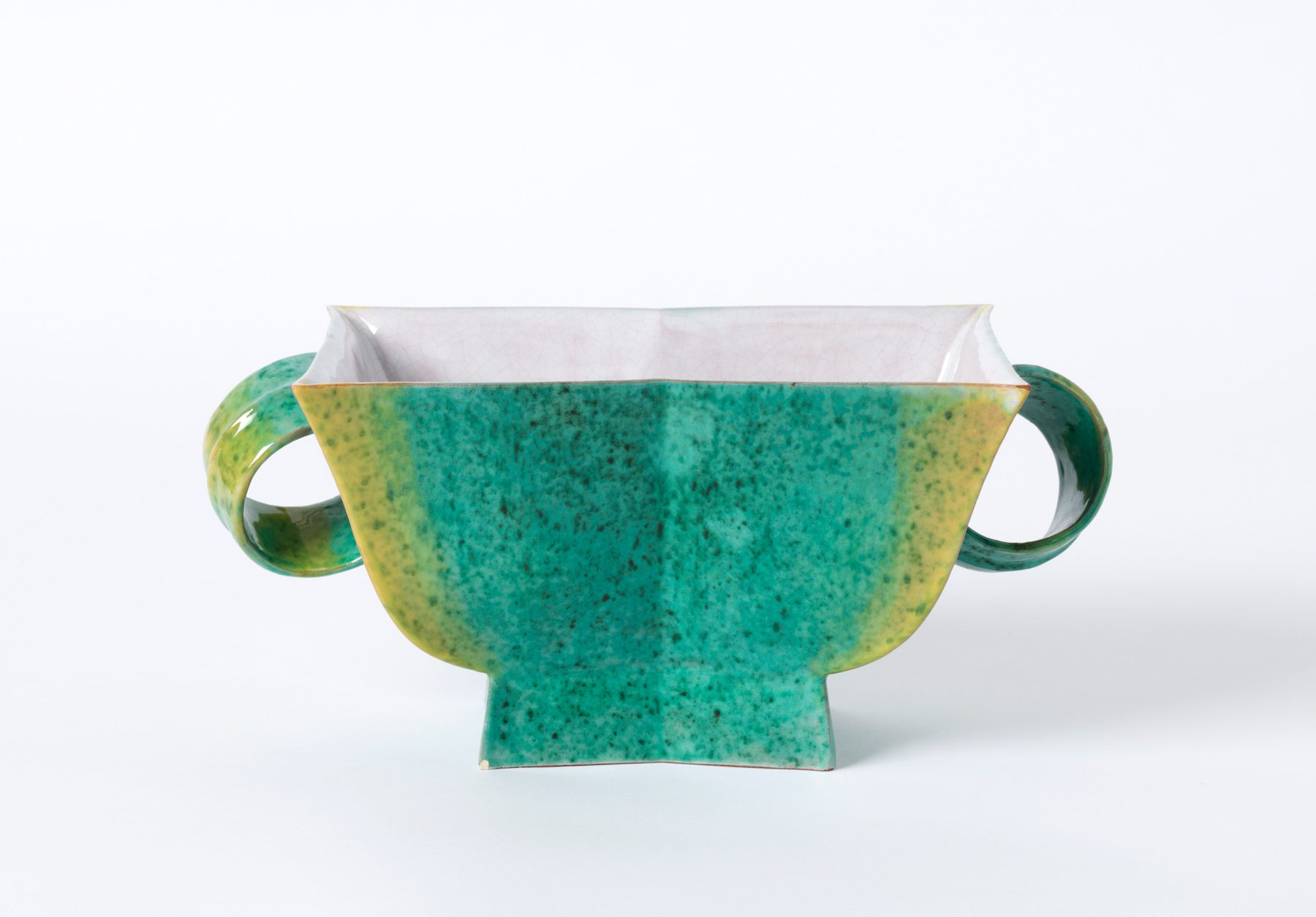 Ceramic vessel with an angular shape, curved handles and a green and yellow speckled glaze.