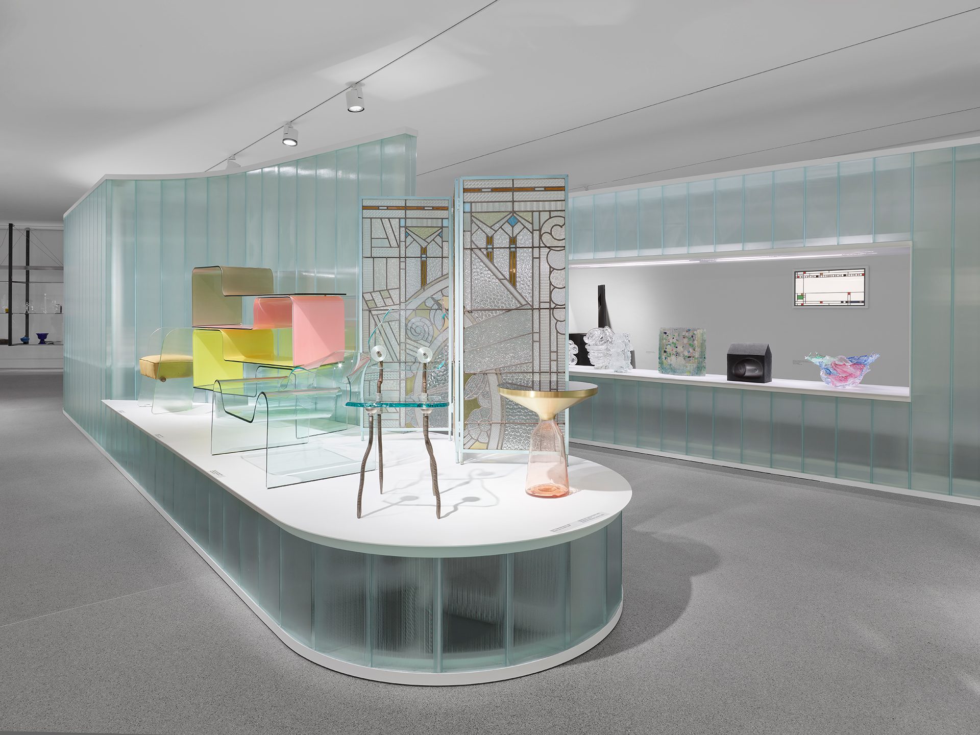 Man sieht die Ausstellungsinstallation "Die Farbe von Glas" bestehend aus gläsernen Wand- und Bodenelementen in der verschiedene Objekte aus Glas gezeigt werden.
