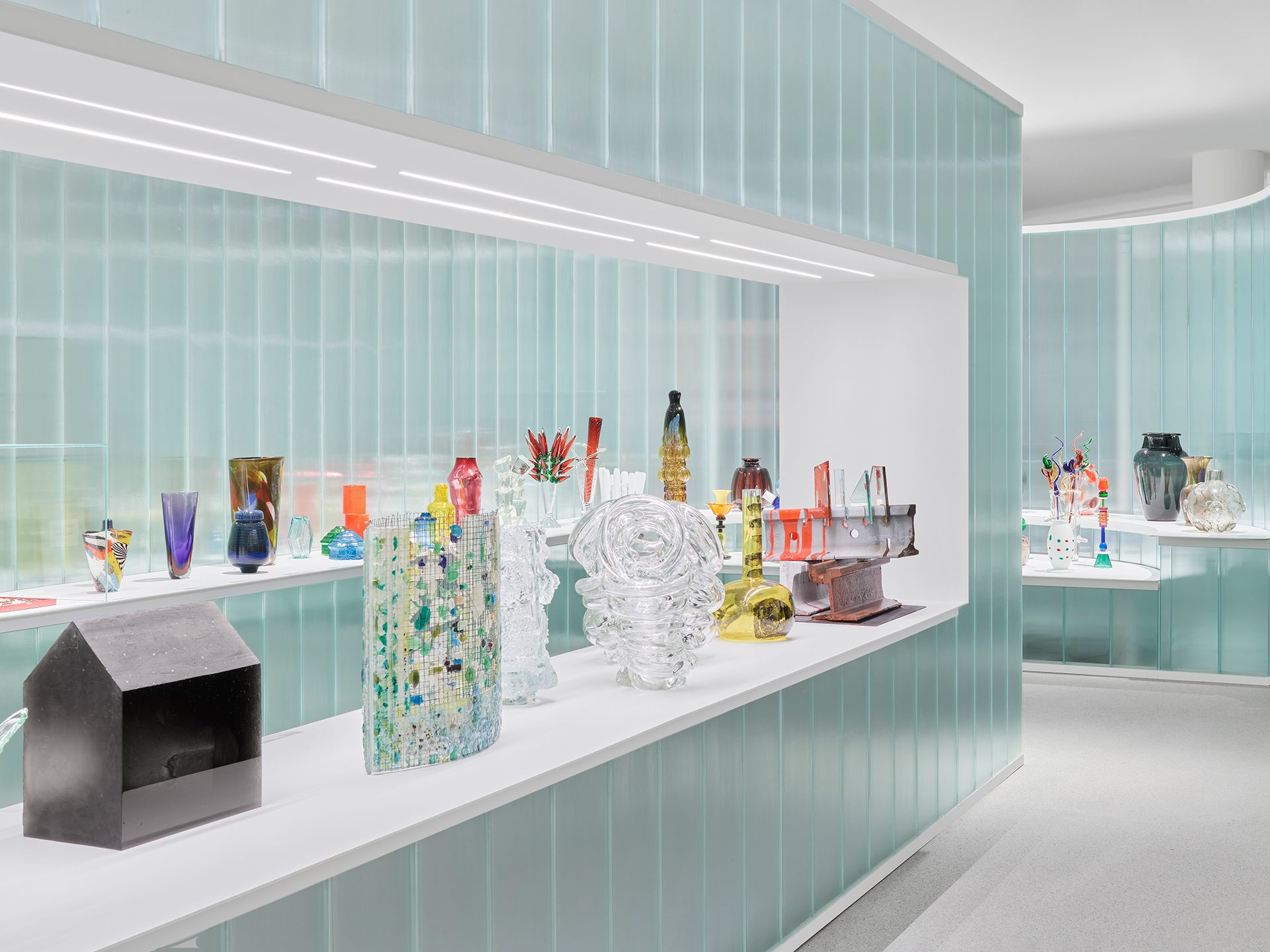 Man sieht die Ausstellungsinstallation "Die Farbe von Glas" bestehend aus gläsernen Wand- und Bodenelementen in der verschiedene Objekte aus Glas gezeigt werden.