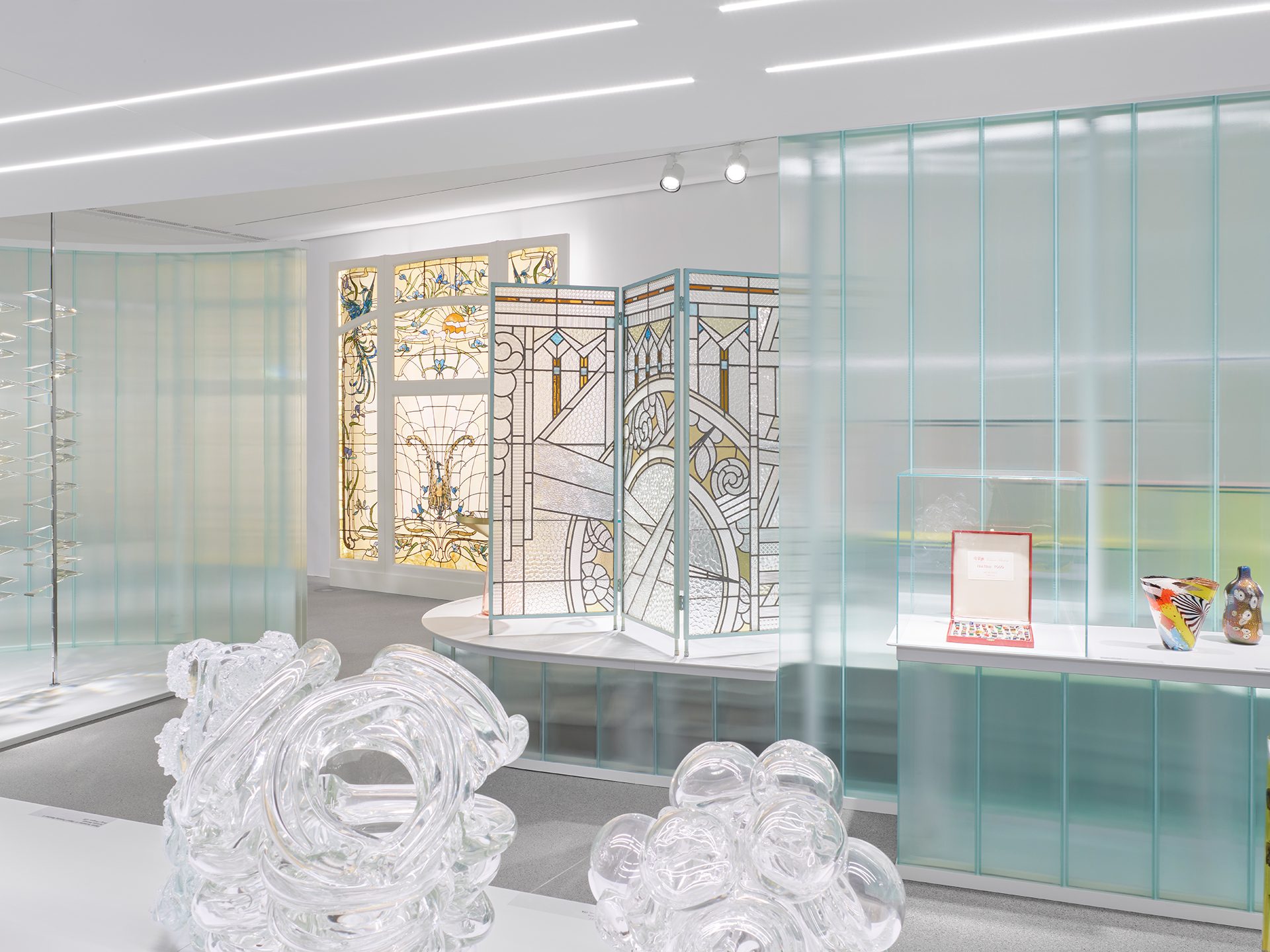 Man sieht die Ausstellungsinstallation "Die Farbe von Glas" bestehend aus gläsernen Wand- und Bodenelementen in der verschiedene Objekte aus Glas gezeigt werden.