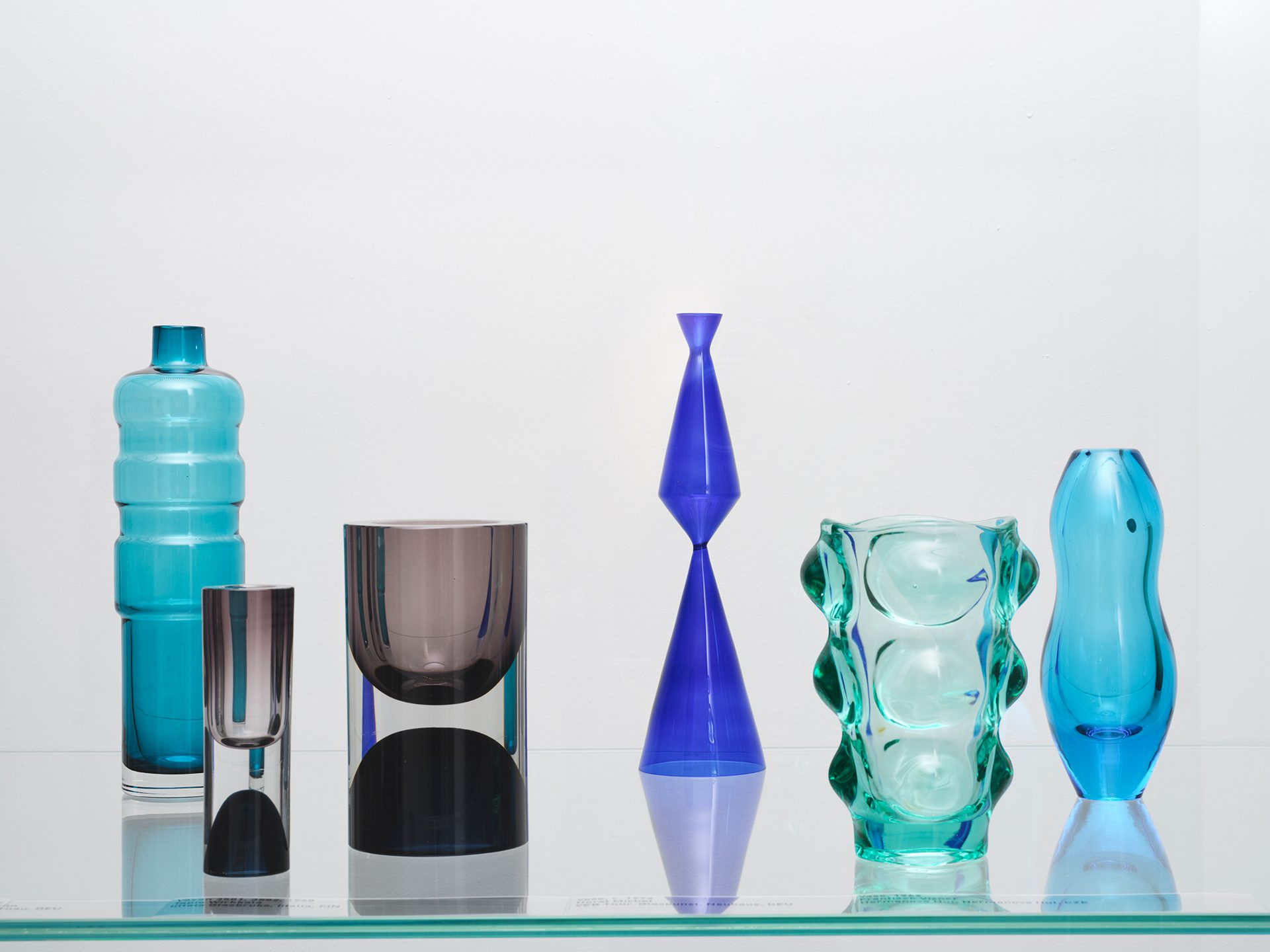 Man sieht die Ausstellungsinstallation "Die Farbe von Glas" bestehend aus gläsernen Wand- und Bodenelementen in der verschiedene Objekte aus Glas gezeigt werden.