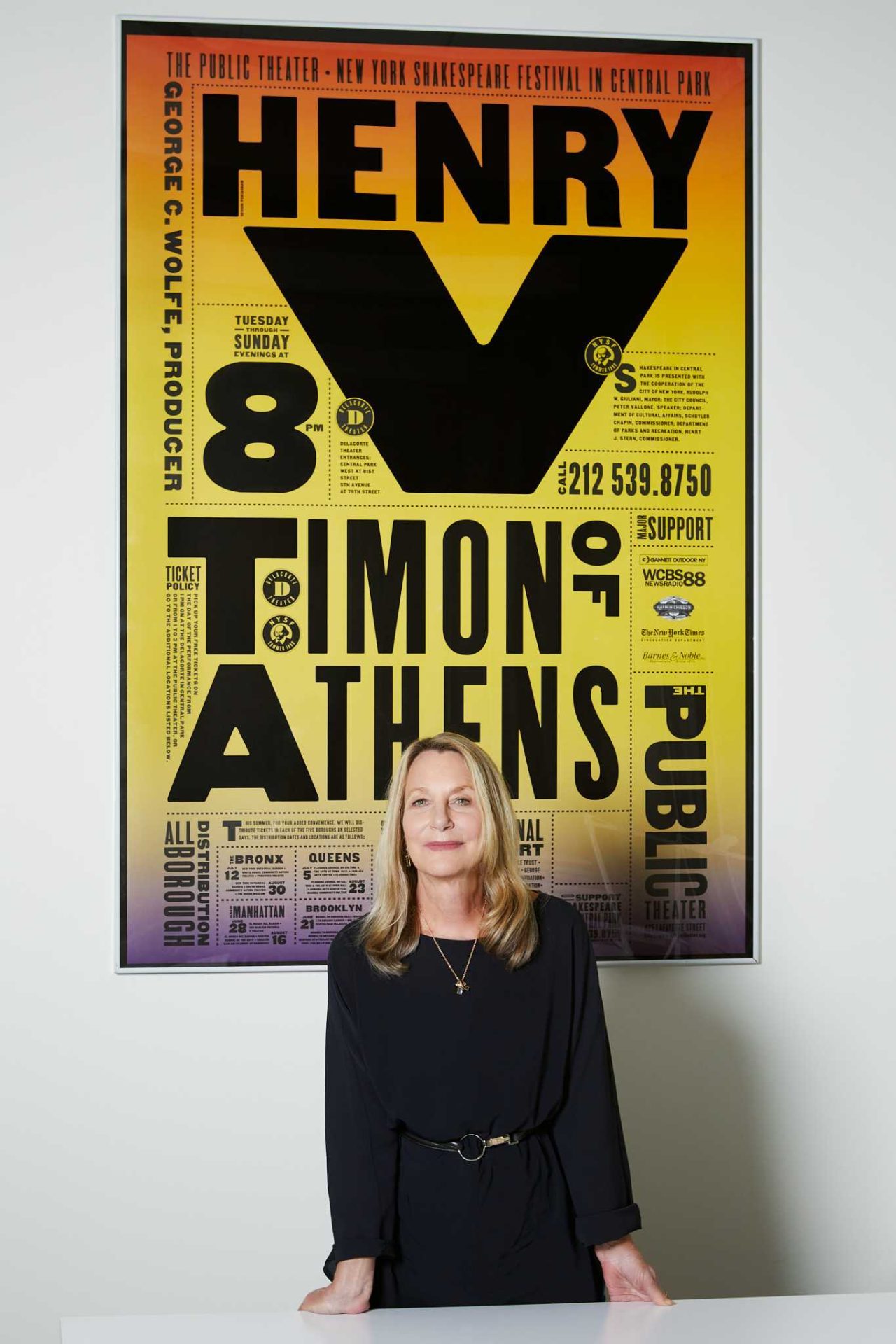 Das Foto zeigt Paula Scher an einem Tisch stehend. Im Hintergrund hängt ein von ihr gestaltetes Festivalplakat.