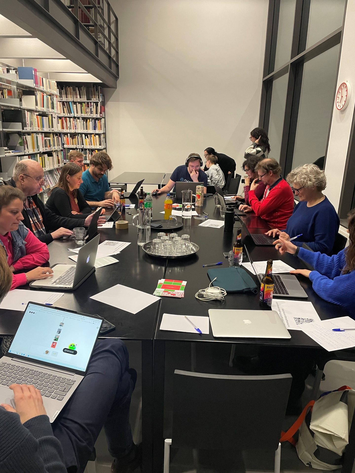 Eine Gruppe von Menschen sitzt an einem großen schwarzen Tisch mit Laptops und Tablets. In der Mitte stehen Getränke.