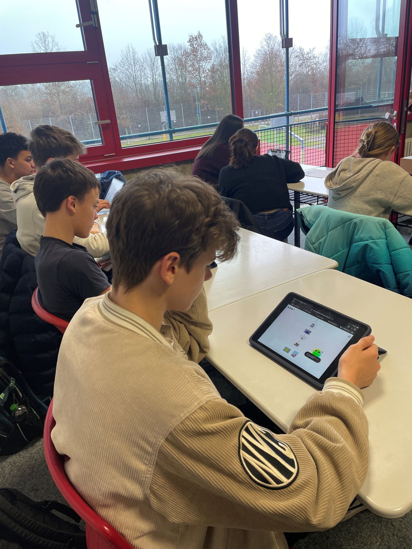 Blick über die Schulter eines Schülers, der das Game spielt. Im Hintergrund weitere Schüler*innen.