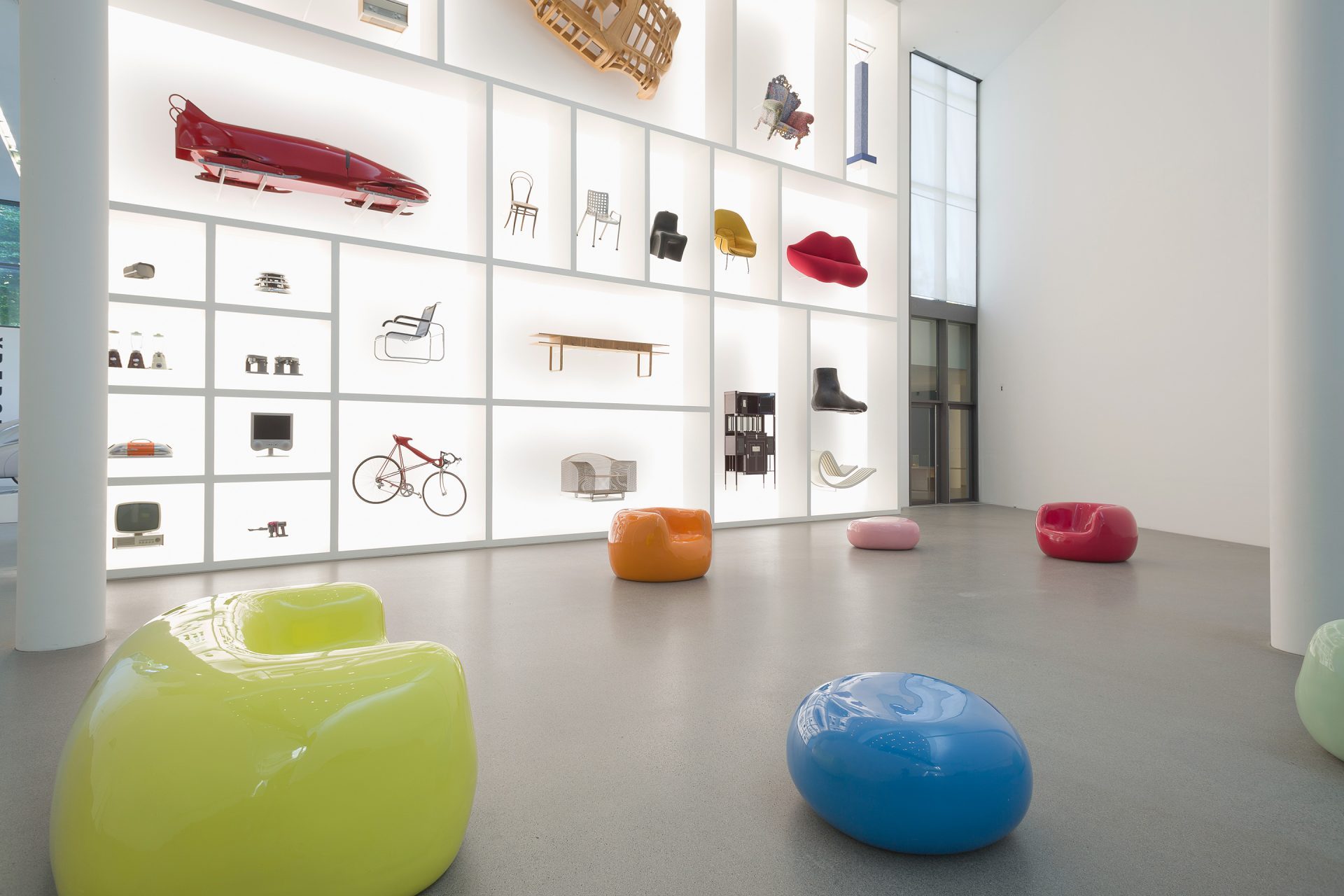 Five colourful seating sculptures in yellow, blue, orange, pink and red in front of the display case.