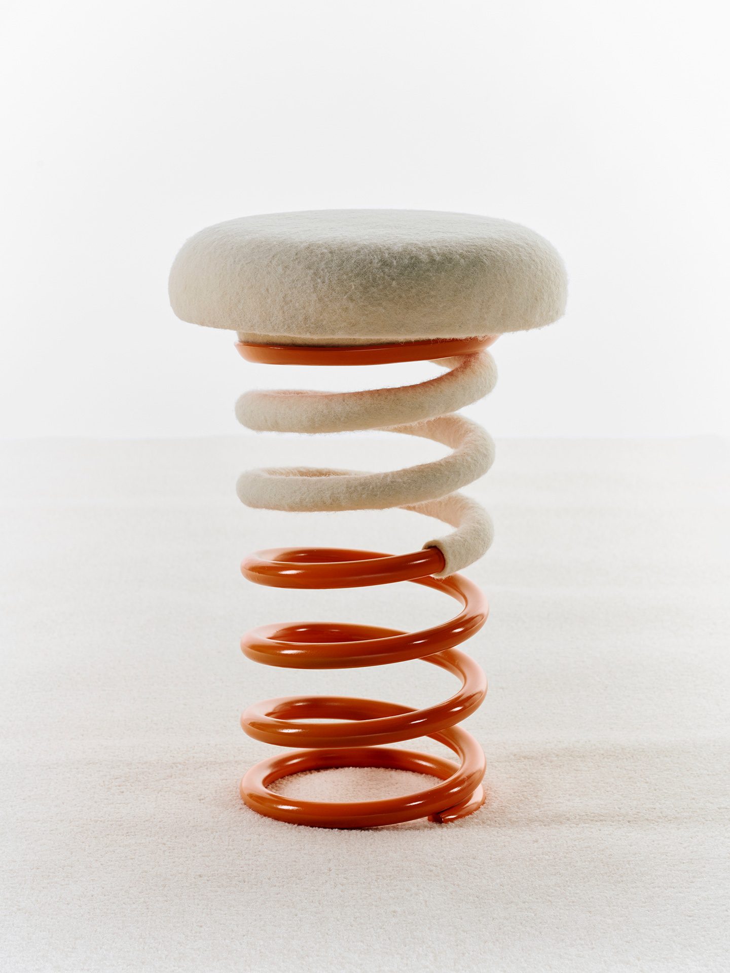 Hocker mit hell bezogener Sitzfläche mit rot lackiertem Fuß in Form einer Stahlfeder.