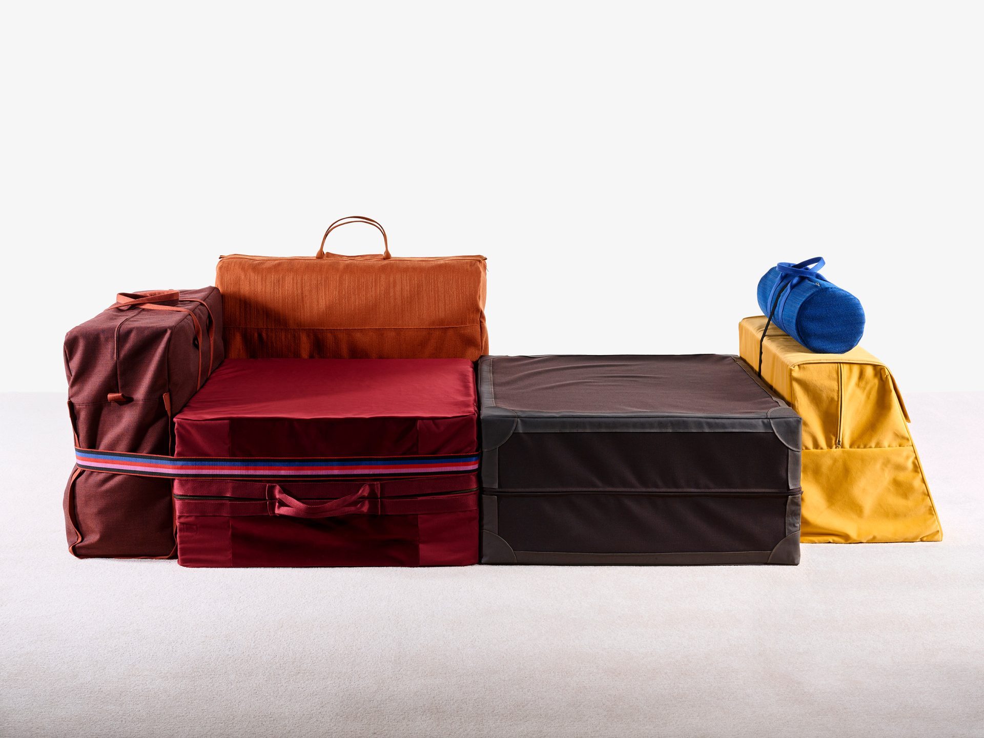 Aus verschiedenfarbigen Taschen mit Tragegriffen zusammengesetztes Sofa.