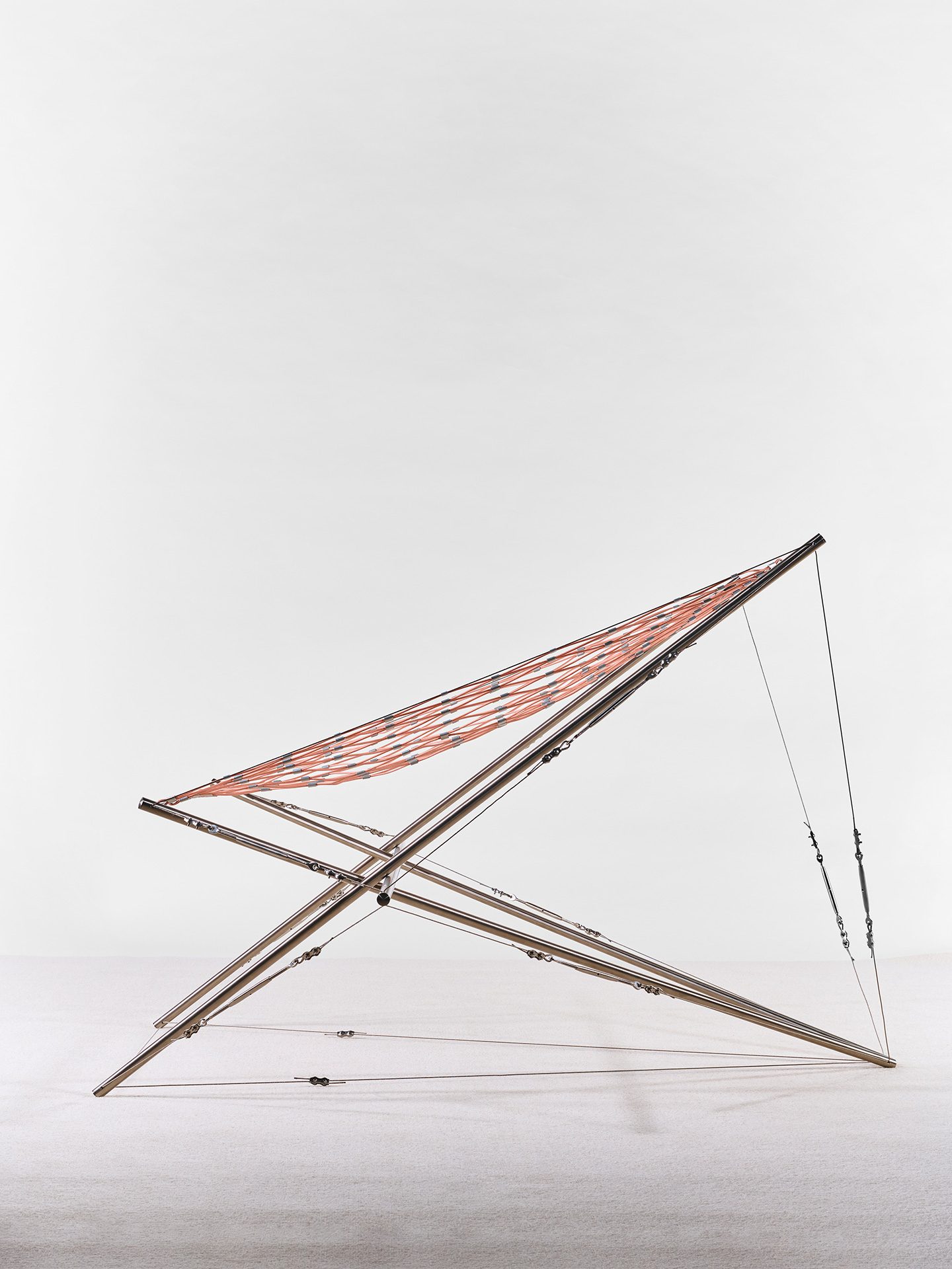 Sessel mit Rahmen aus Edelstahlrohren der von Stahlseilen gehalten wird. Die Sitzfläche ist Netz aus Kunststoff.