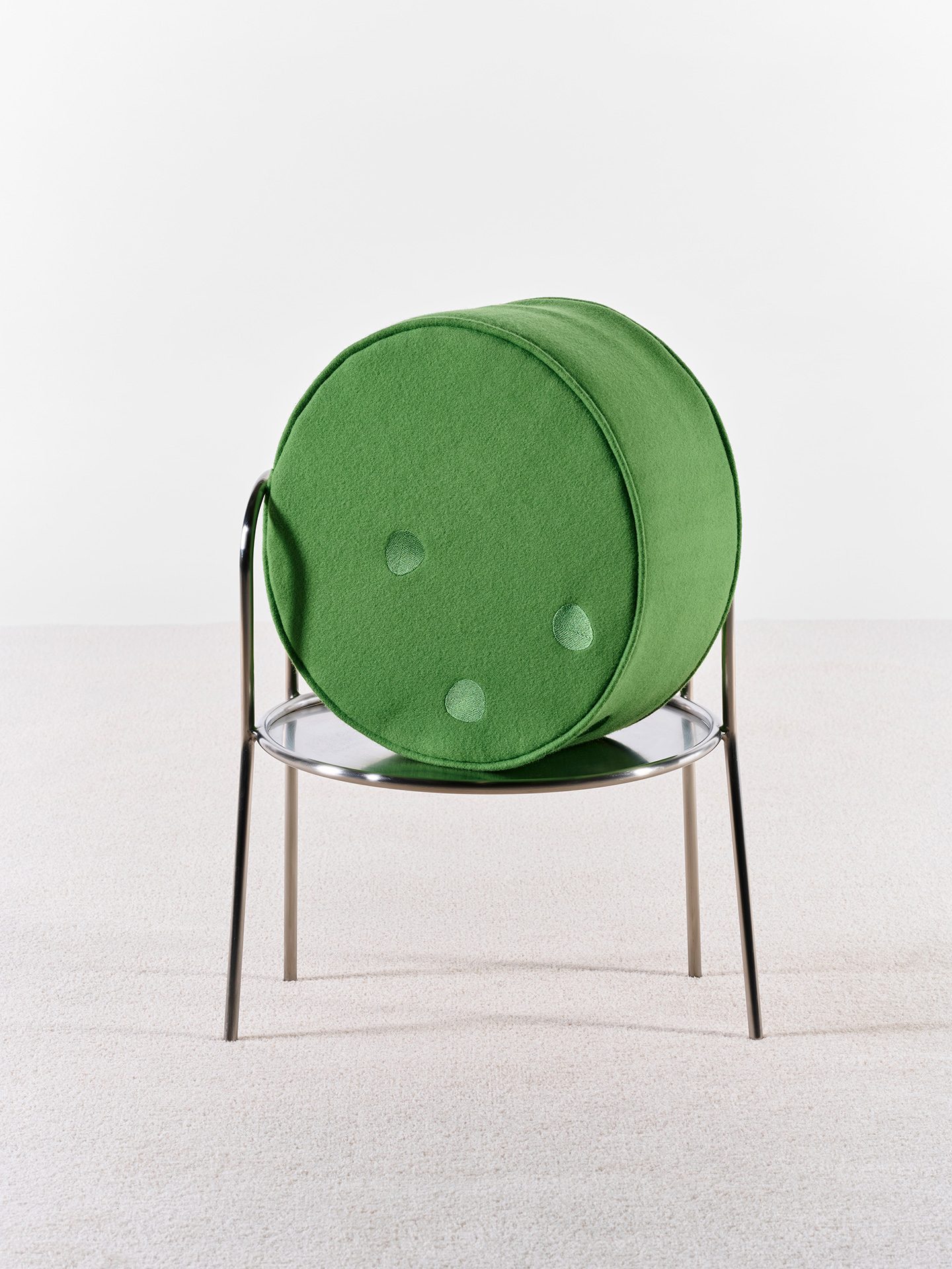 Sessel mit Gestell aus runden Metallrohren und kreisförmiger Sitzfläche mit einem grünen Wollsitzkissen.