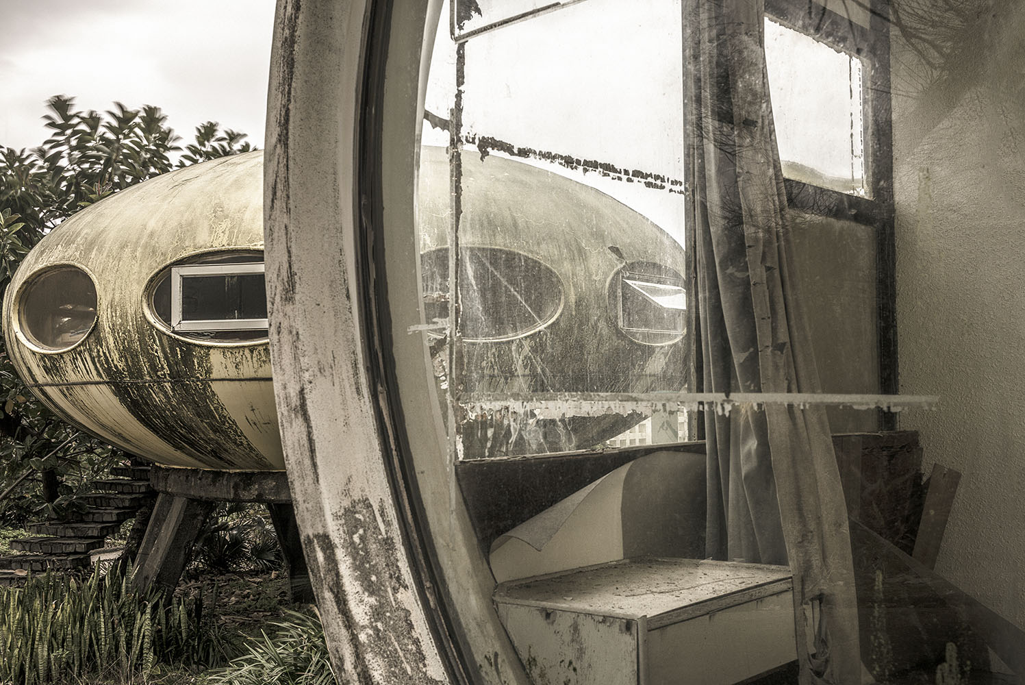 View through a heavily weathered replica of the Futuro plastic house towards another one with a concrete plinth and steps.